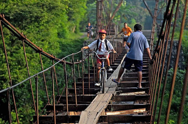 Children from a Javanese village in Indonesia ride their bicycles over narrow planks spanning an between Suro Village and Plempungan Village